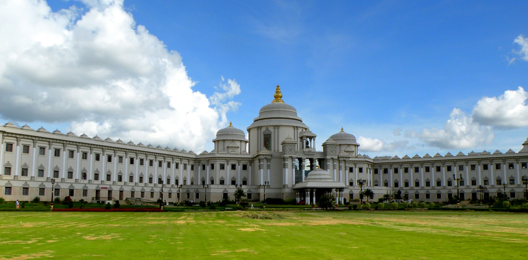 A grand white institutional building across a green lawn in India