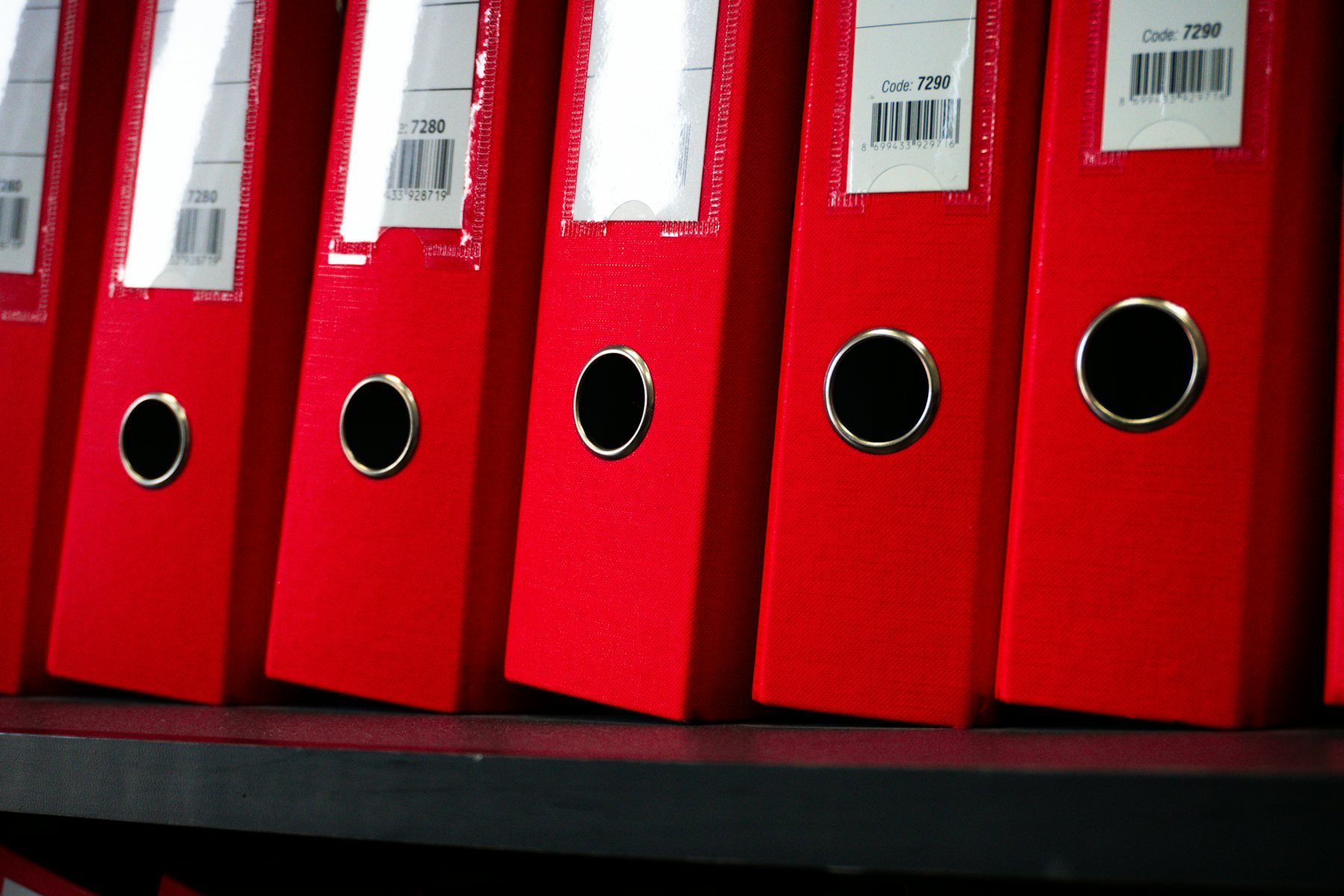 Red archive binders with barcode labels on a shelf